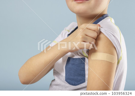Vaccinated kid boy showing arm with adhesive bandage after vaccine injection Vaccinated kid boy showing arm with adhesive bandage after vaccine injection 103956324