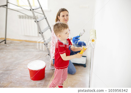 Mother and child son paint the wall with paint using roller and brush 103956342