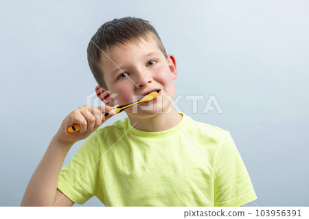 A child in t-shirt brushing teeth with toothbrush on blue background 103956391