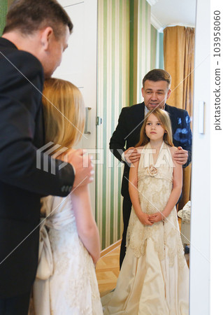 dad and little blonde teenage girl in her mother's wedding dress by the mirror. dad and little blonde teenage girl in her mother's wedding dress by the mirror. 103958060