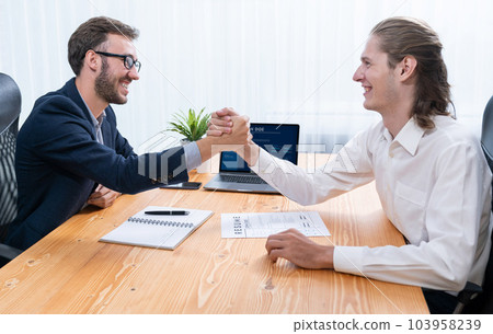 Two happy businessmen shake hands over resume papers. Entity 103958239
