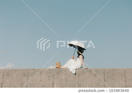 A woman standing on the embankment with a parasol 103963648