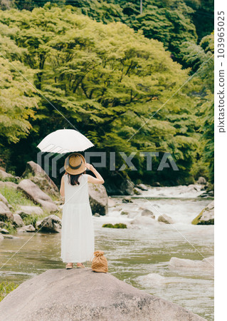 A woman standing by a mountain stream with a parasol 103965025