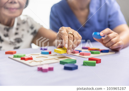 Caregiver and senior woman playing wooden shape puzzles game for dementia prevention 103965287