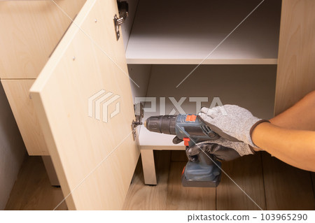 Worker fixing cabinet door hinge on kitchen cabinets Worker fixing cabinet door hinge on kitchen cabinets 103965290