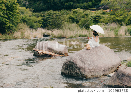 在山澗中拿著帶遮陽傘的智能手機的女人 103965788