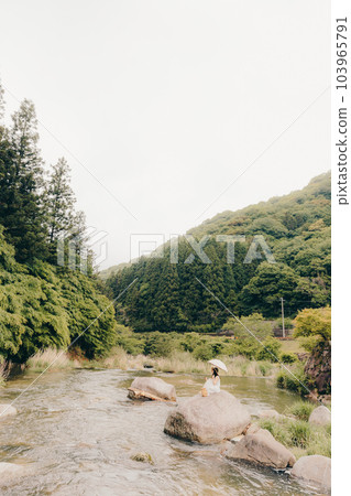 A woman holding a smartphone with a parasol in a mountain stream A woman holding a smartphone with a parasol in a mountain stream 103965791