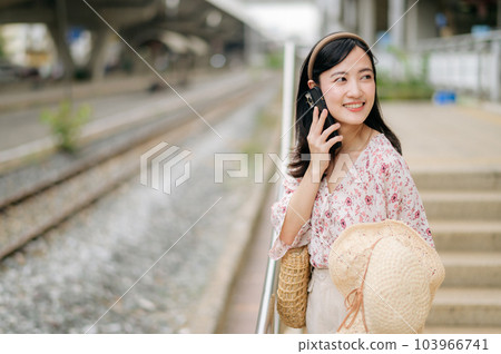 Asian young woman traveler with weaving hat using a mobile phone beside railway train station in Bangkok. Journey trip lifestyle, world travel explorer or Asia summer tourism concept. Asian young woman traveler with weaving hat using a mobile phone beside railway train station in Bangkok. Journey trip lifestyle, world travel explorer or Asia summer tourism concept. 103966741