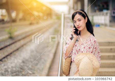 Asian young woman traveler with weaving hat using a mobile phone beside railway train station in Bangkok. Journey trip lifestyle, world travel explorer or Asia summer tourism concept. Asian young woman traveler with weaving hat using a mobile phone beside railway train station in Bangkok. Journey trip lifestyle, world travel explorer or Asia summer tourism concept. 103966742
