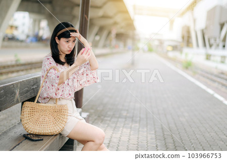 young asian woman traveler checking her face in a mirror and waiting for train in train station. Journey trip lifestyle, world travel explorer or Asia summer tourism concept. 103966753