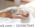 Closeup woman Hand of a patient with medical drip or IV drip lying on bed in hospital, Patient with drip receiving a saline solution. free space for text 103967045