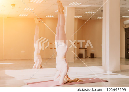 Young sporty woman, fitness instructor in pink sportswear doing stretching and pilates on yoga mat in the studio with mirror. Female fitness yoga routine concept. Healthy lifestyle and harmony. 103968399
