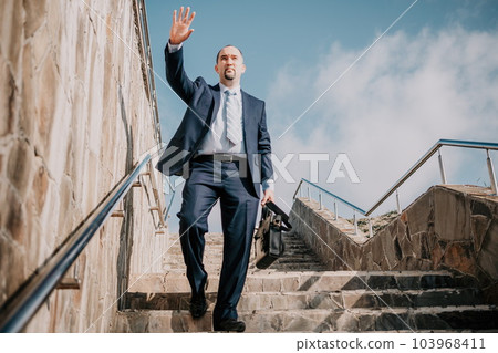 Confident middle age businessman with briefcase walking upstairs. Close-up of businessman wearing blue suit holding bag walking down the stairs Confident middle age businessman with briefcase walking upstairs. Close-up of businessman wearing blue suit holding bag walking down the stairs 103968411