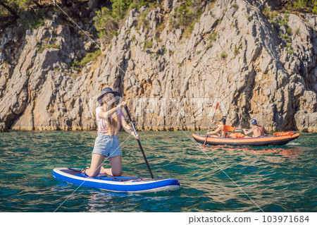 Young women Having Fun Stand Up Paddling in blue water seaamong the rocks in Montenegro. SUP 103971684