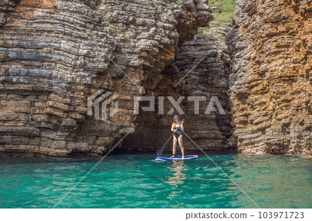Young women Having Fun Stand Up Paddling in blue water seaamong the rocks in Montenegro. SUP 103971723