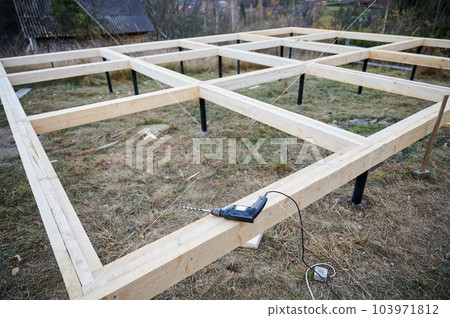 Drill laying on wooden pile foundation for future frame house. Constuction site and work instrument concept. 103971812