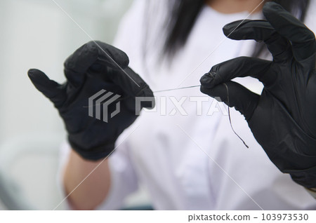 Close-up dental floss in the hands of a doctor dentist, dental hygienist wearing black surgical gloves. The concept of dental health and oral hygiene. Dentistry. Hygiene. Healthcare and medicine 103973530