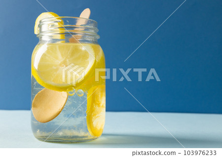 Close-up of mason jar with lemonade and lemon slices on table against blue background, copy space 103976233