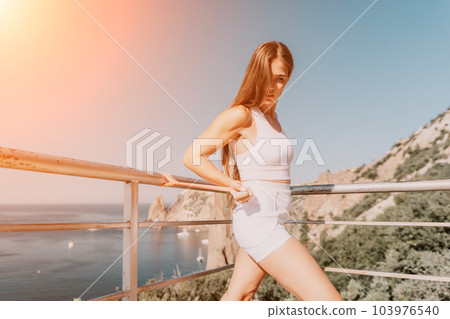 Woman sea fitness. Happy woman with long hair, fitness instructor in white doing stretching and pilates with ribbons in park near the sea. Female fitness yoga routine concept. Healthy lifestyle. 103976540