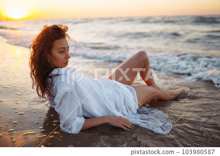 Stylish woman in elegant white dress posing near the sea. People, freedom, lifestyle, travel. 103980587