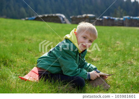 Fun teenager sits on hillside. Boy resting in mountains. School boy sitting of hill in grass field and enjoying beautiful landscape view. Rear view of teenage boy hiker resting in nature. Active Fun teenager sits on hillside. Boy resting in mountains. School boy sitting of hill in grass field and enjoying beautiful landscape view. Rear view of teenage boy hiker resting in nature. Active 103981601