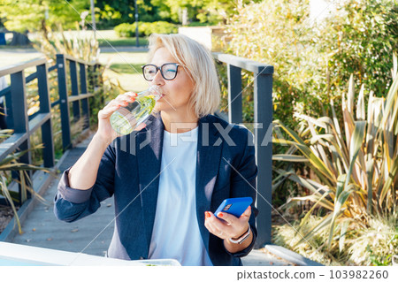 Healthy habit to drink water. Smiling middle aged business woman with bottle of water with lemon and mint during her outdoor lunch break. Control body hydration, Tracker water balance. Healthy living Healthy habit to drink water. Smiling middle aged business woman with bottle of water with lemon and mint during her outdoor lunch break. Control body hydration, Tracker water balance. Healthy living 103982260