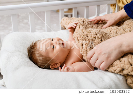 Female hands cover a newborn baby with blanket in crib 103983532