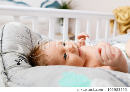 Cute infant baby laying on his back in a wooden cot. 103983533