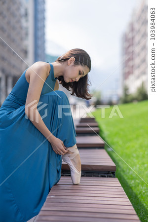 Beautiful asian ballerina in blue dress adjusting her pointe shoes outdoors. Beautiful asian ballerina in blue dress adjusting her pointe shoes outdoors. 103984063