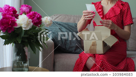 Young woman buyer opening parcel box at home. Female customer shopper receiving online shop purchase buying cream unpacking delivery package. Young woman buyer opening parcel box at home. Female customer shopper receiving online shop purchase buying cream unpacking delivery package. 103984083