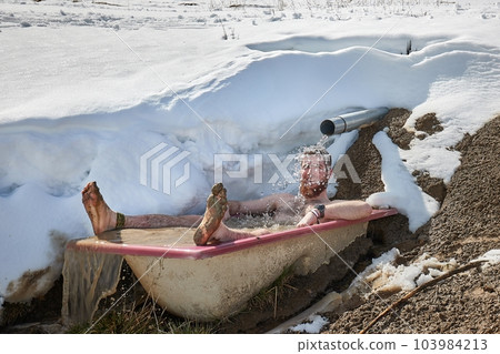 Man taking cold plunge in a snowy bathtub 103984213