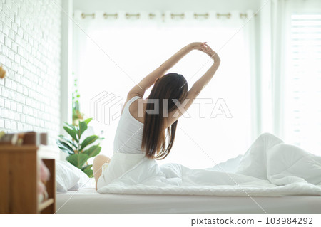 Back of view Woman stretching her arm after wake up on bed and looking outside windows in bedroom feeling so fresh and relax in the morning,Healthcare Concept 103984292