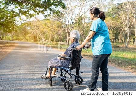 Caregiver help and care Asian elderly woman on wheelchair at park with happy in holiday. 103986015