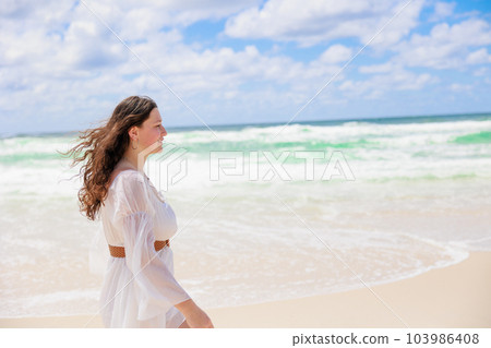 一位身穿白色連衣裙的白人女孩在沙灘上散步的概況 一位身穿白色連衣裙的白人女孩在沙灘上散步的概況 103986408