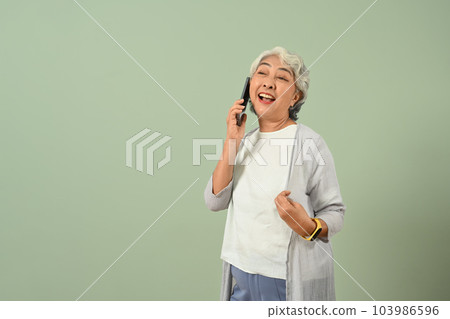 Joyful elderly female talking on mobile phone isolated on green background. People, communication and modern technology 103986596