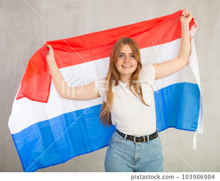 smiling girl in arms raised above head holds canvas of national flag of Netherlands 103986984