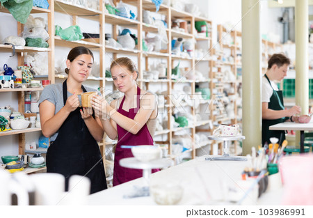 Young woman examines ceramic cup made by teenage girl Young woman examines ceramic cup made by teenage girl 103986991