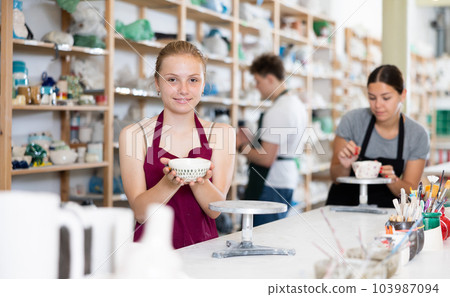 Satisfied teenager girl shows cup created by himself in clay workshop Satisfied teenager girl shows cup created by himself in clay workshop 103987094