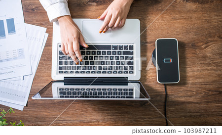 Charging mobile phone battery with wireless charging device in the table. Smartphone charging on a charging pad. Mobile phone near wireless charger Modern lifestyle technology concept. Charging mobile phone battery with wireless charging device in the table. Smartphone charging on a charging pad. Mobile phone near wireless charger Modern lifestyle technology concept. 103987211