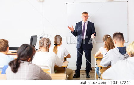 Male teacher at whiteboard during lesson with teen students 103987241