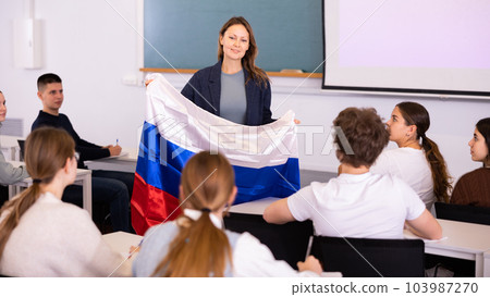 Female teacher tells her classmates about the country of Russian, holding flag in her hands Female teacher tells her classmates about the country of Russian, holding flag in her hands 103987270