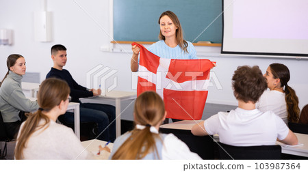 Adult female teacher showing the flag of Denmark to the students 103987364