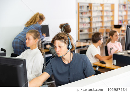 Portrait of a fifteen-year-old schoolboy in headphones at a computer 103987384