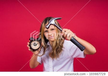 Young blonde girl holding alarm clock and hammer smiling and laughing hard out loud. Young blonde girl holding alarm clock and hammer smiling and laughing hard out loud. 103987729