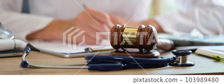 Court gavel with stethoscope on a table in background doctor writes notes Court gavel with stethoscope on a table in background doctor writes notes 103989480