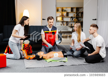 Young man instructor helping to make first aid heart compressions with dummy during the group training indoors 103989883