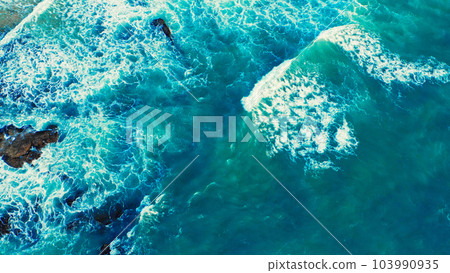 Beautiful blue ocean waves - aerial view. Top view to the beautiful azure water sea surface. Atlantic Ocean, Portugal. Drone view of rolling waves with white foam on the summer sunny day. Beautiful blue ocean waves - aerial view. Top view to the beautiful azure water sea surface. Atlantic Ocean, Portugal. Drone view of rolling waves with white foam on the summer sunny day. 103990935