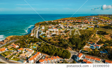 Aerial view of a small European town against blue sky and Atlantic Ocean. Drone view of a beautiful European city with a hilly landscape on ocean background. Beautiful natural landscape. Portugal. 103990950