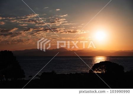 Picturesque view Sunrise From Corfu Island Overlooking Mountains Of Balkan Peninsula Of Greece, Moraitika, Corfu. In Foreground Are Silhouettes Of Trees And Water Slide. 103990990