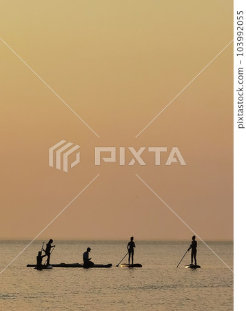 Group of people on stand up paddle board at quiet sea on sunset or sunrise. People on sup board and bright sunset 103992055